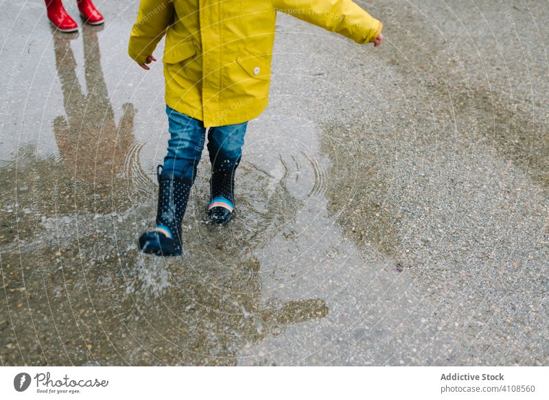 Anonymous funny kids playing in puddle in park alley children messy weather together siblings season water wet dirt childhood mud game active rubber boots
