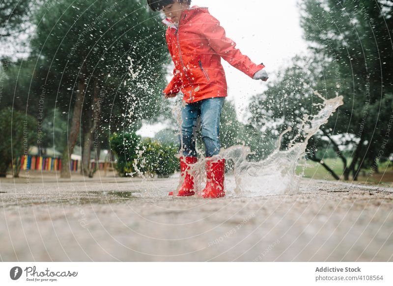 Active kid jumping in puddle in park alley child messy season funny water wet dirt childhood weather mud autumn game active rubber boots raincoat botanical