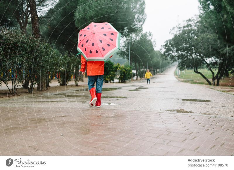 Cute child with colorful umbrella walking in park alley rain season funny water wet dirt childhood mud autumn game active weather rubber boots raincoat