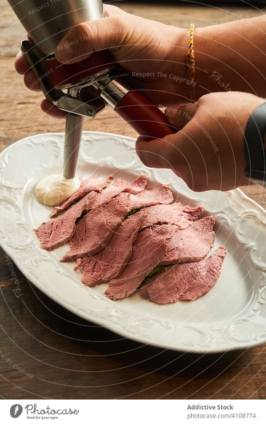 Crop chef pouring sauce into dish of roast beef cook slice steak plate serve food roasted dinner meal lunch fresh recipe cafe table dishware delicious piece