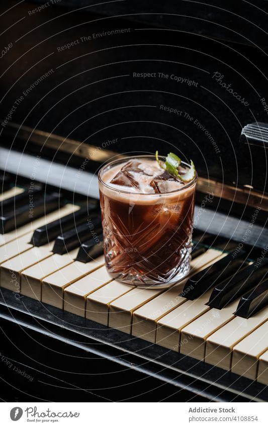 Glass of cocktail with ice resting on a piano keys drink beverage hand pub restaurant bar mint foam fresh classic relax art yummy music modern harmony colorful