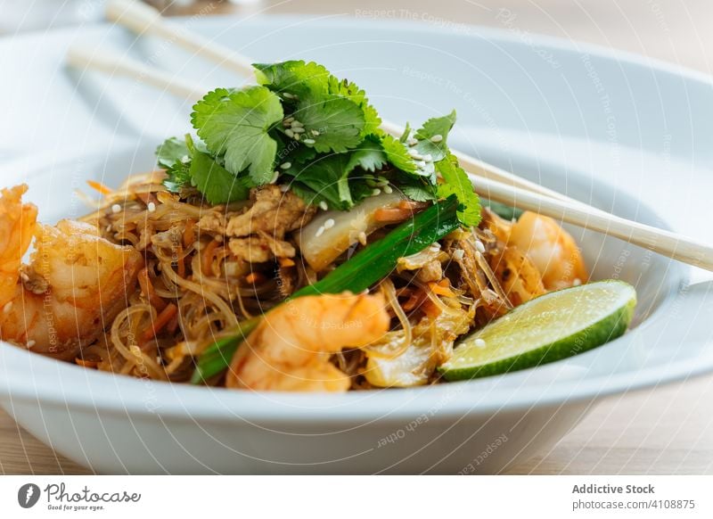 Asian dish of noodles with shrimps in restaurant chopsticks asian food haute cuisine lime greenery herb parsley seafood plate wooden organic tasty table fresh