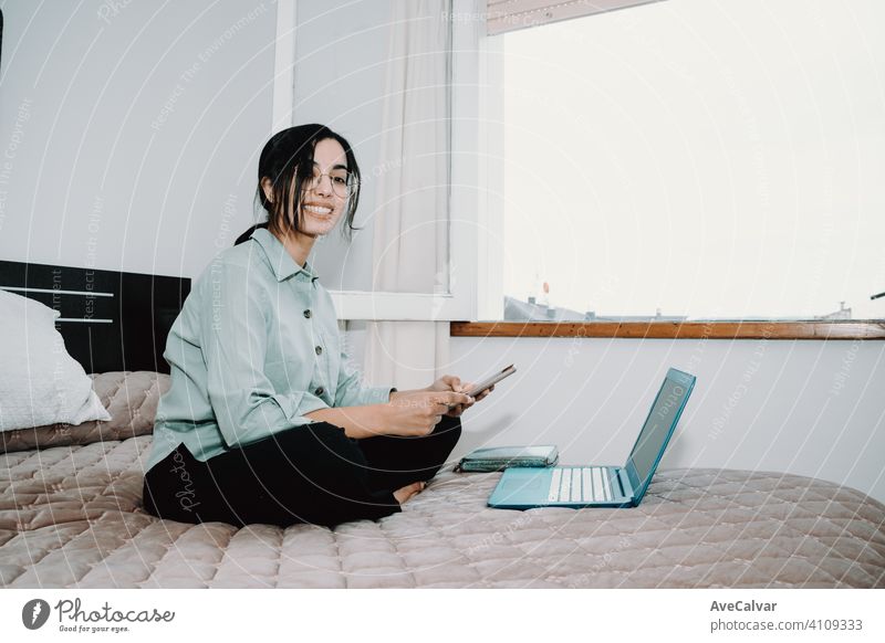 Young arab woman working at home on his laptop while using his phone over his bed with copy space technology sitting room girl young computer female indoors