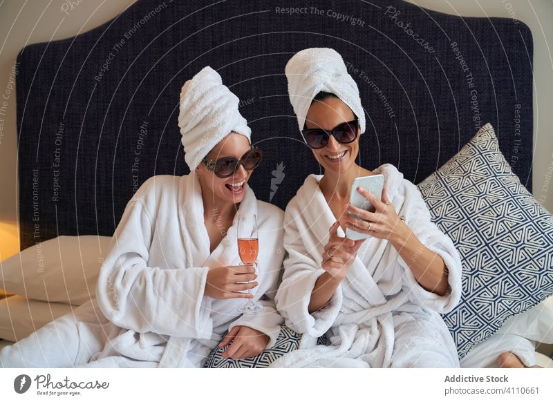 Friends using smartphone while relaxing in bedroom together at pajama party friends photography beverage celebrate smile happy bathrobe vacation satisfied chill
