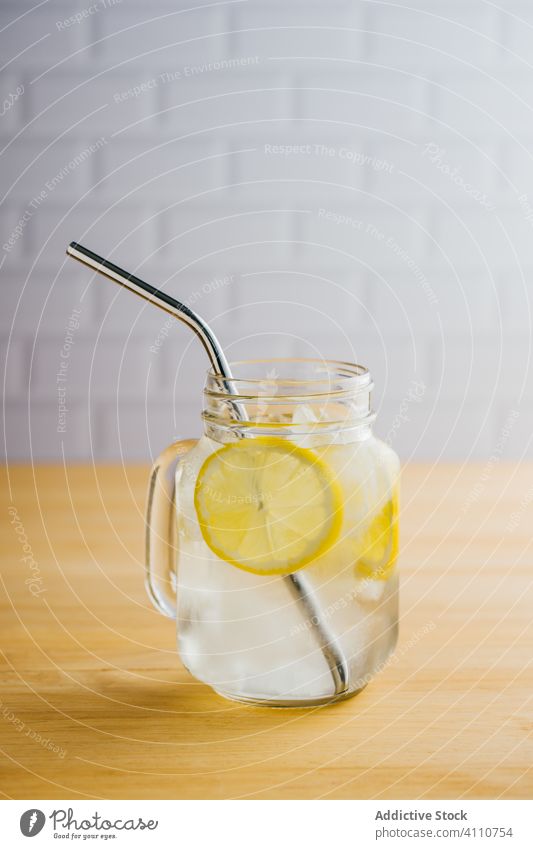 Glass jar with ice and straw on table lemon metallic reusable glass jug slice wooden eco friendly reject kitchen fresh beverage cold drink fruit lemonade water