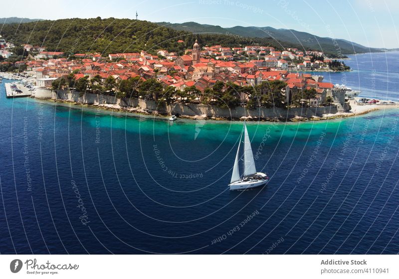 Sailboat on sea near aged town on island sailboat ocean blue old ancient historic water travel vacation tourism picturesque yacht Croatia city nature vessel