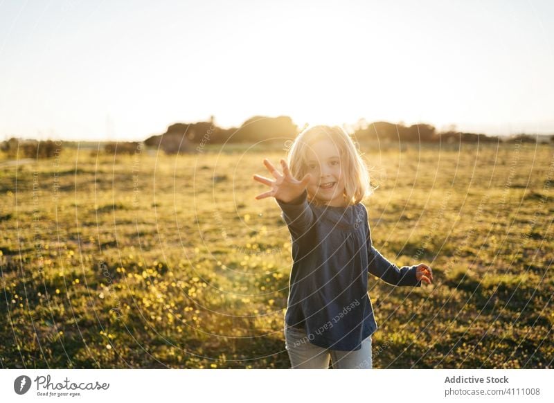 Cheerful little girl standing in field in summer evening kid happy nature child enjoy having fun sunset smile playful outstretch gesture finger meadow