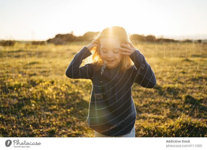 Cheerful little girl standing in field in summer evening kid happy nature child enjoy having fun sunset smile playful outstretch gesture finger meadow