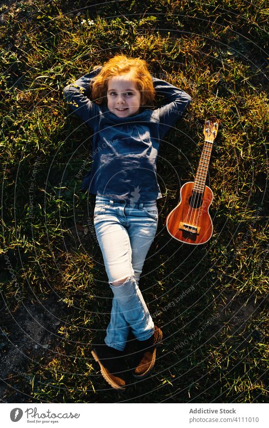 Little girl lying down on grass with ukulele kid play music guitar nature tree child summer little instrument sound song melody trunk perform practice rest