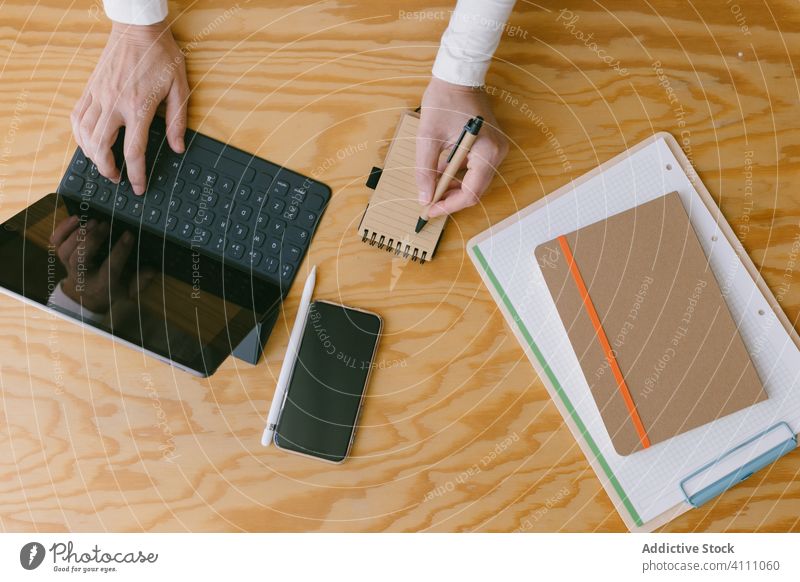 Faceless businesswoman with tablet and notepad workplace write take note wood occupation device keypad typing keyboard using surfing browsing internet workspace
