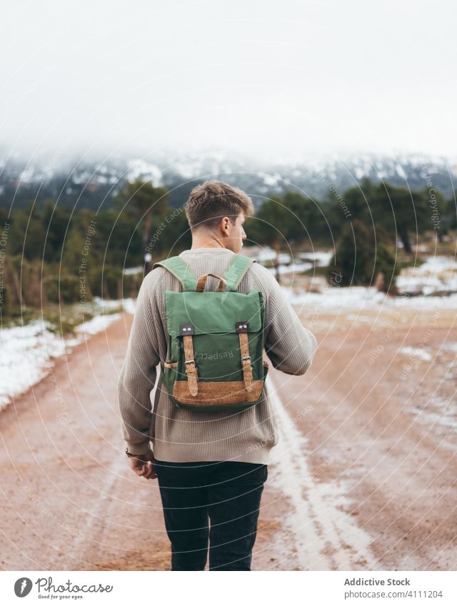 Man with backpack walking on rural road man travel countryside nature journey dirt adventure cold autumn winter snow forest male freedom tourism destination