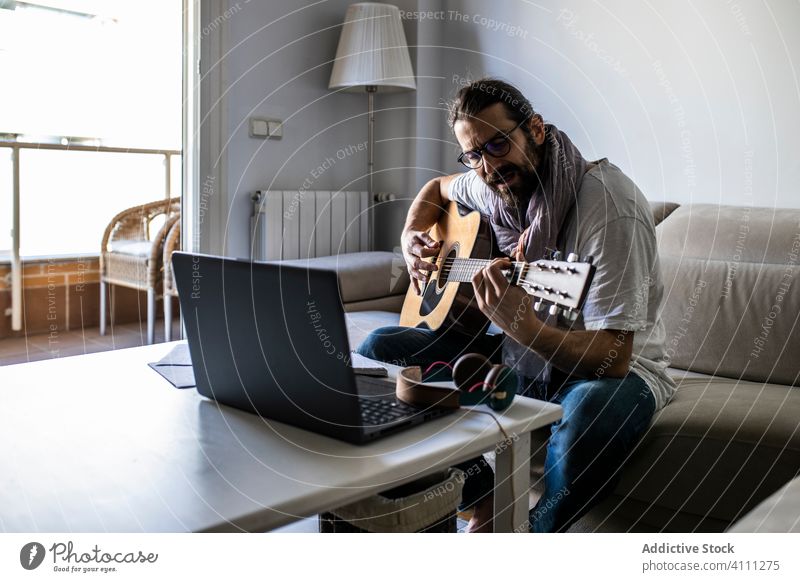 Stylish guitarist on couch in living room man play sit sofa male casual music songwriter composer poet home lifestyle talent instrument melody perform lesson