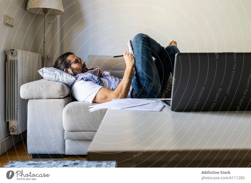 Man writing notes on couch in cozy living room man write sofa male casual comfort songwriter lying poet composer relax home apartment young pillow rest read
