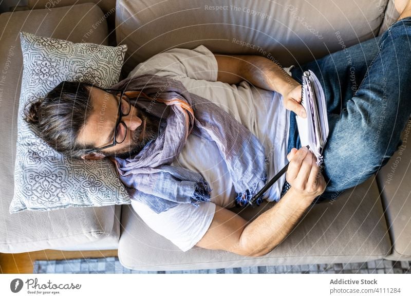 Man writing notes on couch in cozy living room man write sofa male casual comfort songwriter lying poet composer relax home apartment young pillow rest read
