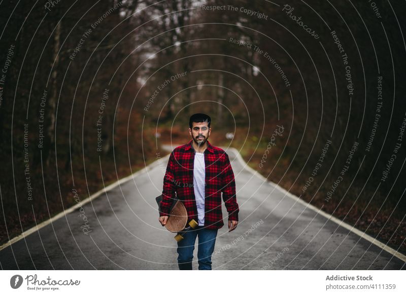 Male skater on road among autumn forest man skateboard countryside casual walk style male tree empty asphalt nature freedom adventure season way activity