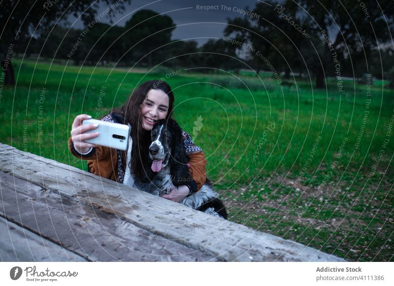 Satisfied lady taking selfie on smartphone with dog in park woman smile laugh enjoy female mobile spaniel hug embrace animal cuddle green summer love friend