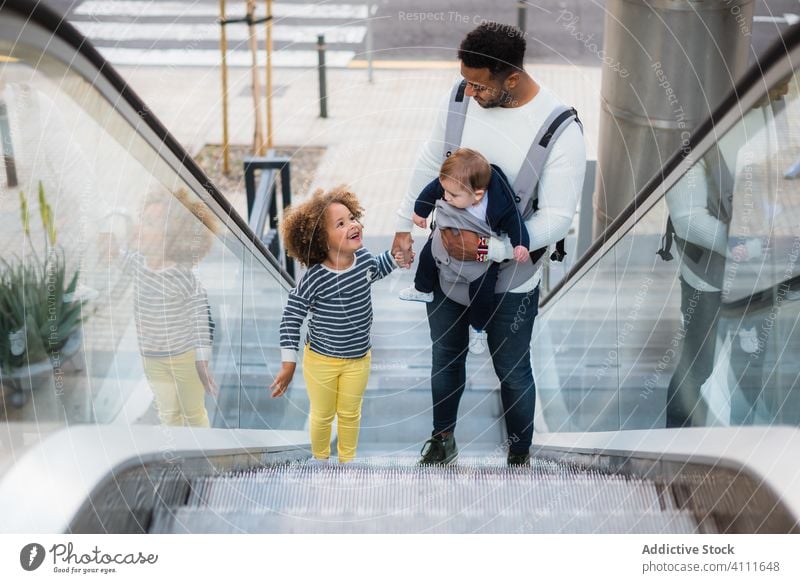 Ethnic father with kids on escalator man together daughter son happy urban city trendy love relationship male casual stair modern sibling cheerful smile style