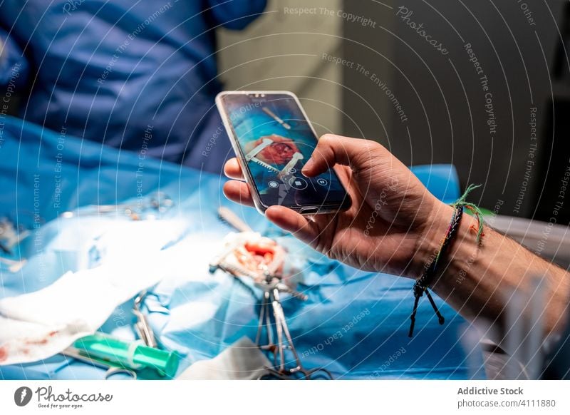 Man taking shot with smartphone while medical staff operating patient in contemporary clinic surgeon surgery hospital hand mobile phone photography