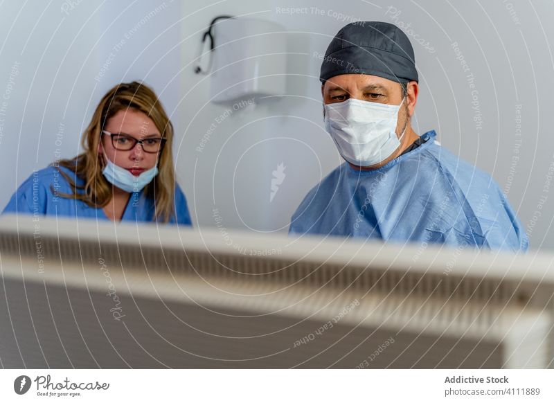 Doctor and assistant checking information on screen while performing diagnostic patient disease in contemporary clinic colleague uniform hospital doctor