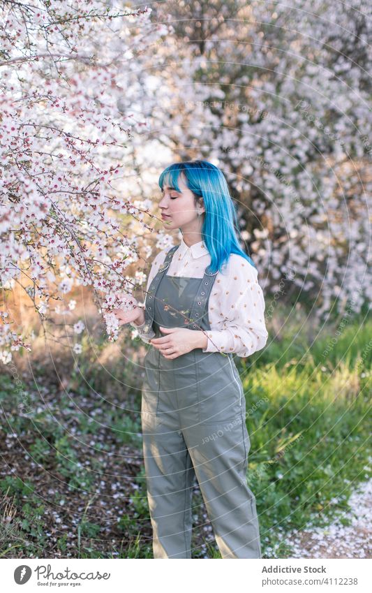 Trendy woman in blooming garden spring teen smell fragrance alternative dyed hair flower style trendy modern young blue hair blossom tree female nature floral