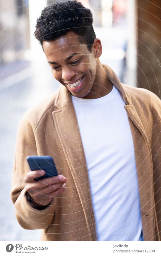 Young black man using his smartphone outdoors. male cuban young person smiling happy student casual lifestyle t-shirt adult guy african portrait cellphone