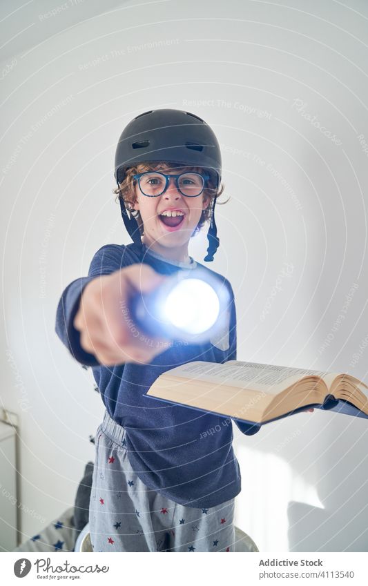 blond kid in pajamas with a helmet a flashlight and a book playing research children game protect happiness enjoyment room indoor party comfort emotional