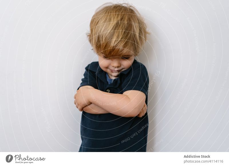 Upset child showing grimace while standing on white wall kid little boy preschool childhood expressive home cute innocent son copy space looking down