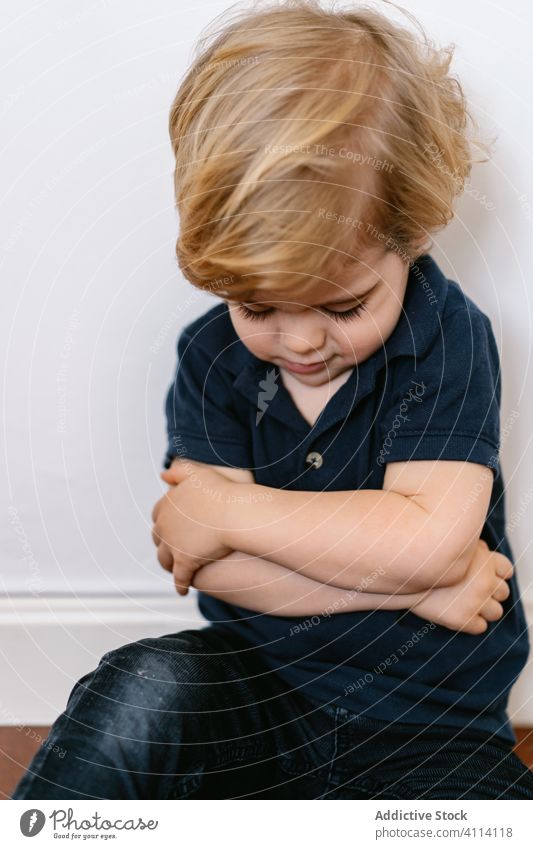 Upset child showing grimace while sitting on the floor kid little boy preschool childhood expressive home cute innocent son copy space white background wall