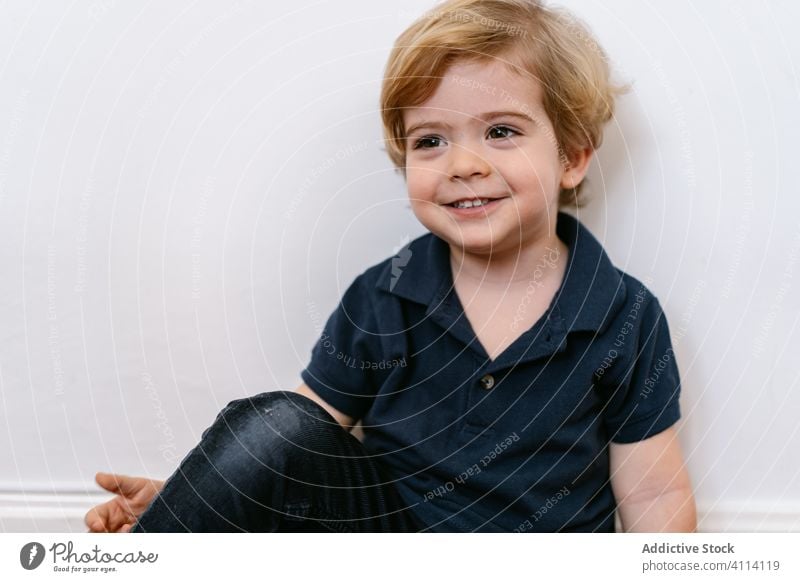 Happy little kid sitting and leaning in a while wall happy boy energy preschool adorable child joy laugh fun childhood expressive playful smile home cute