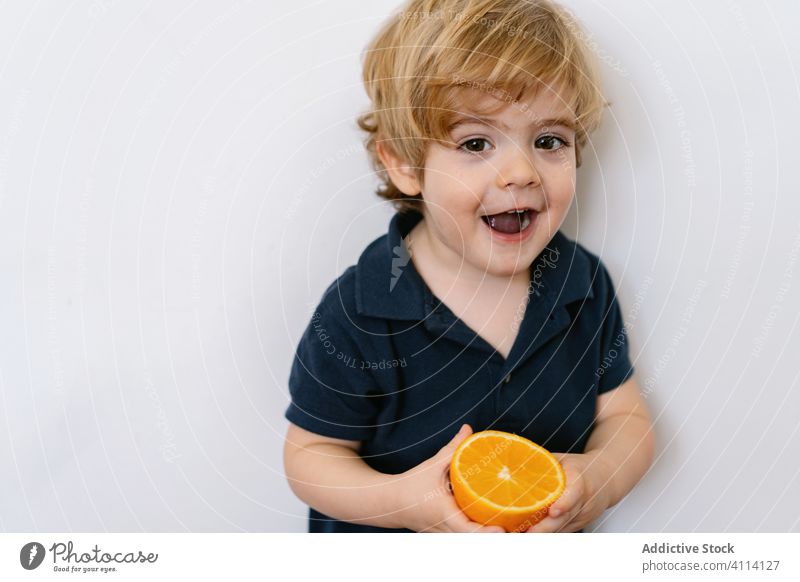 Smiling little kid playing with orange half boy smile playful fruit charming sweet juice funny curious delicious tongue out happy cheerful joy cute healthy