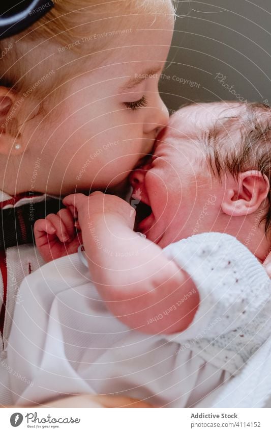 Little girl kissing crying baby newborn sibling love sister care relationship together embrace tender hug neonatal cuddle protect gentle daughter child kid