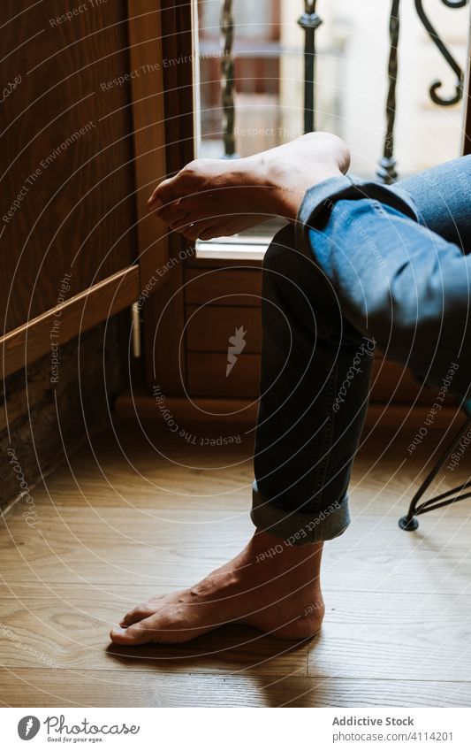 Crop person resting near window home cozy barefoot jeans calm weekend room floor sit morning apartment flat lounge domestic chair relax casual lifestyle