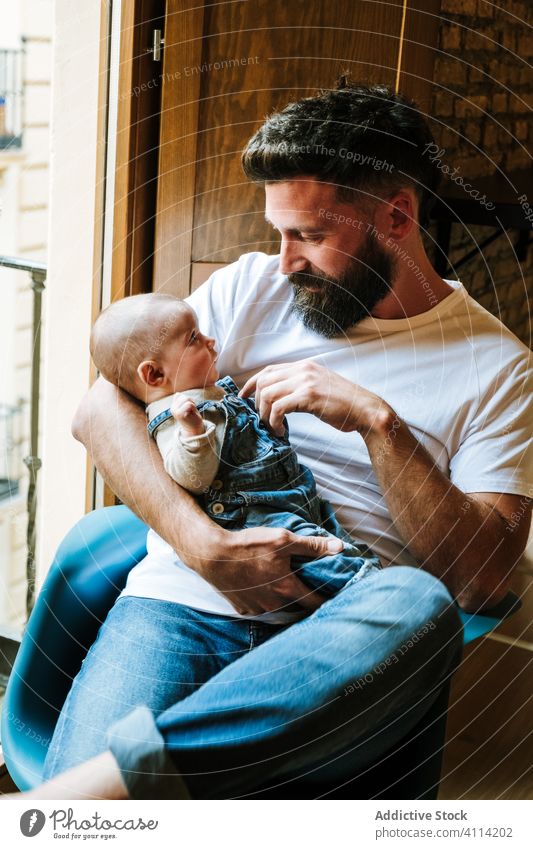 Bearded father communicating with baby communicate hug home love tender window sit cozy chair man infant kid child little embrace parent cuddle close