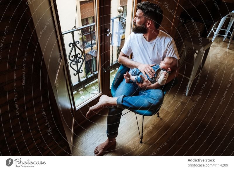 Bearded father with baby sitting near window beard communicate hug home love tender cozy chair man infant kid child little embrace parent cuddle close