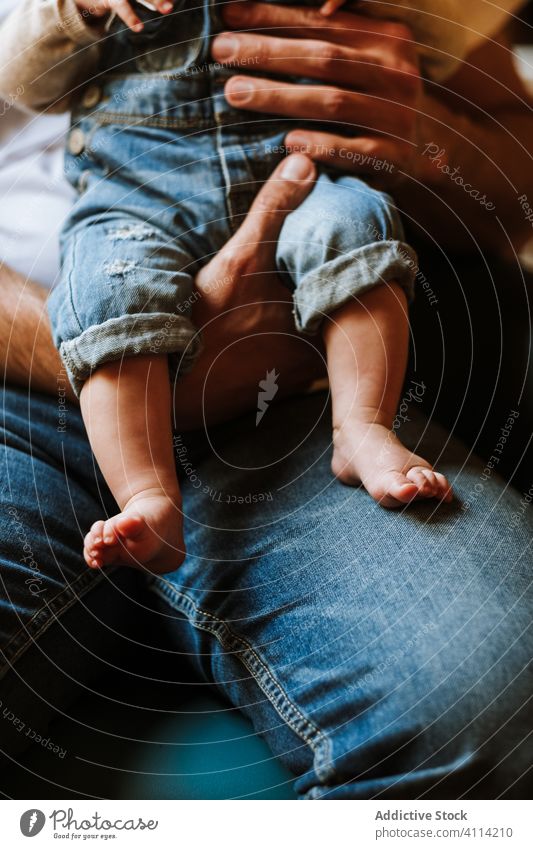 Crop parent with baby resting at home sit chair floor love care cozy room child kid together childhood lounge relax casual jeans barefoot lifestyle domestic