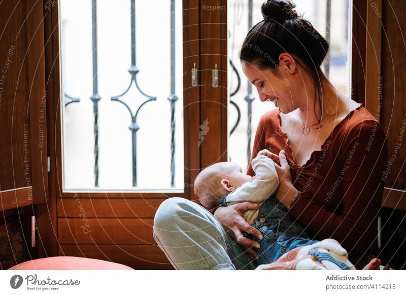 Happy mother breastfeeding baby near window home happy love rest cozy sit cheerful woman cute room hug embrace smile child kid childhood little care together