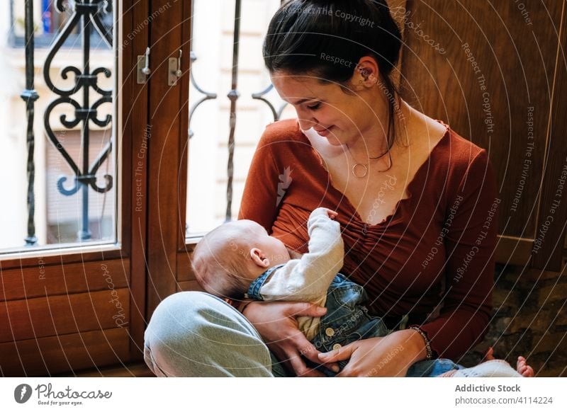 Happy mother breastfeeding baby near window home happy love rest cozy sit woman cute room hug embrace smile child kid childhood little care together parent