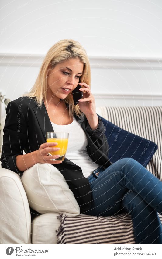 Woman drinking juice and using smartphone on sofa woman home mobile phone rest female social media lounge healthy sit fresh orange browsing couch glass fruit
