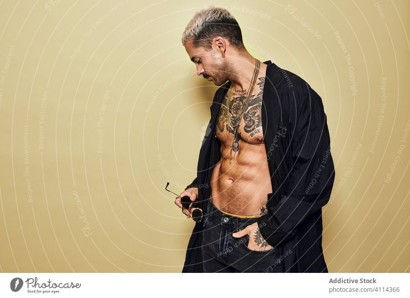 Provocative shirtless man in black coat sunglasses macho cool trendy brutal tattoo style fashion unshaven model personality muscular jeans beard male ethnic