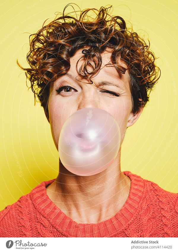 Funny young woman blowing bubble gum sweater orange casual style fun blink curly hair trendy bright female vivid vibrant expressive model colorful cool outfit