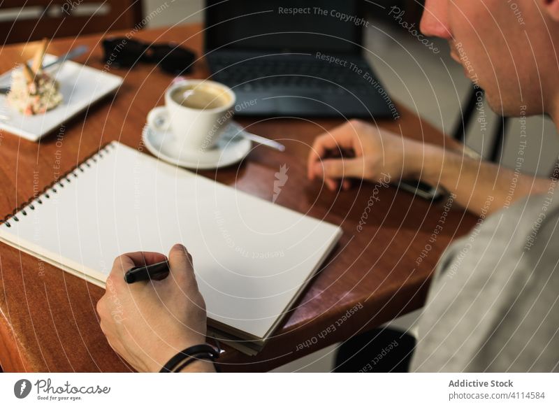 Crop freelancer drawing in notebook in cafe man sketch coffee laptop table remote project male notepad cup student drink cafeteria computer education restaurant