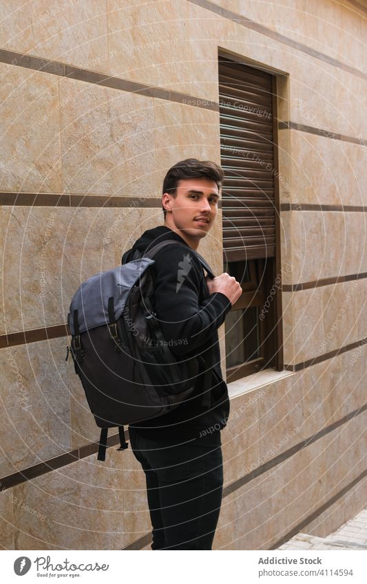 Male student on city street man positive building window wall backpack young male casual modern smile pedestrian urban architecture education confident