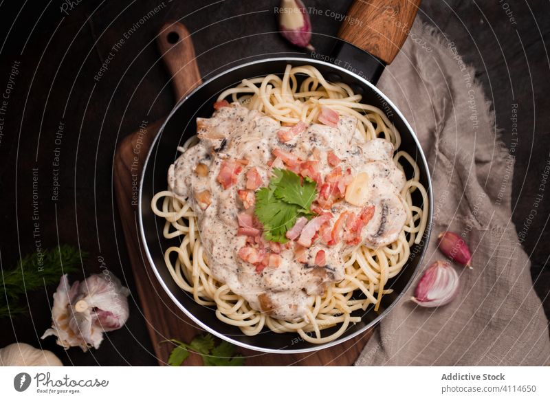 Top view of appetizing pasta with ham and mushrooms in creamy sauce served in frying pan tasty spaghetti cutting board healthy food meal gourmet delicious