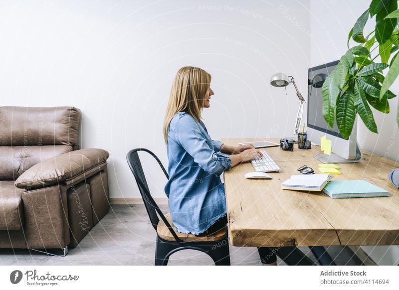 Blonde Caucasian woman works from her home office browsing computer typing desk communication businesswoman tablet indoor adult laptop desktop design lifestyle