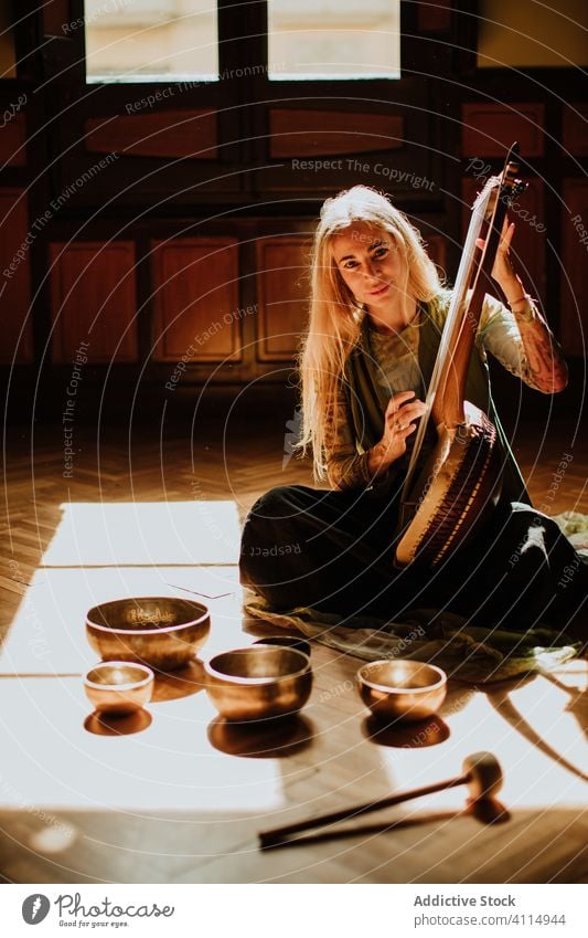 Woman playing lyre near tibetan bowls woman traditional music home floor sit melody female adult cozy room sound hobby art creative talent perform lady retro