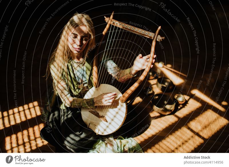 Lady playing lyre in dark room woman traditional music home floor sit blonde tibetan bowl melody adult cozy sound hobby art creative talent perform retro