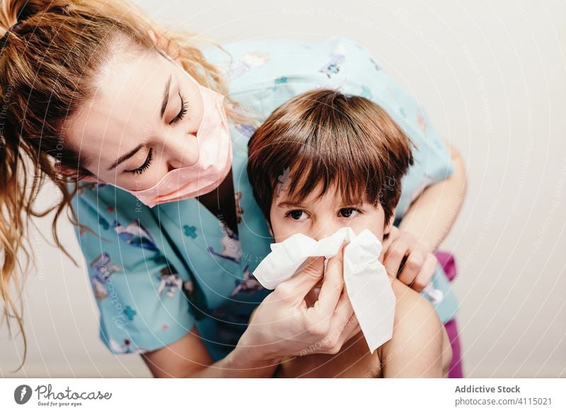 Little boy blowing nose in hospital on check up kid sick bed patient respiratory ill female nurse health care illness treat unwell clinic medical disease little