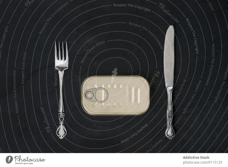 Can with fork and knife on black desk silverware can tin meal preserve conserve board sardine seafood table set creative closed oil fish utensil snack concept