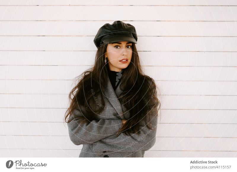 Confident young female near white wall woman style street confident cap building coat outfit model serious urban wear accessory hat brunette headgear exterior