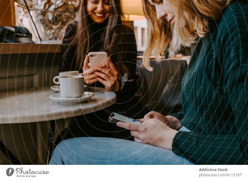 Female friends resting in cozy cafe women laugh together coffee smartphone using joke casual weekend young meeting restaurant drink cup beverage coffee shop